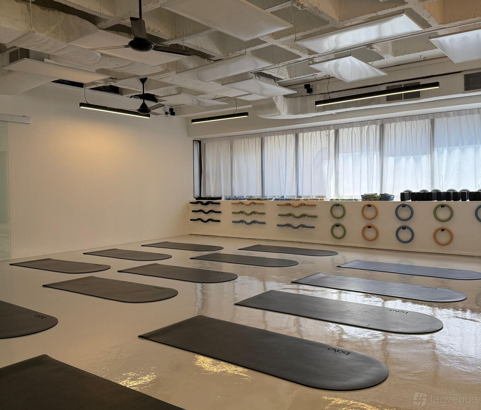A yoga studio with polished floors, wall-mounted props, yoga mats arranged in rows, and large windows at Dopamine Movement Studio.
