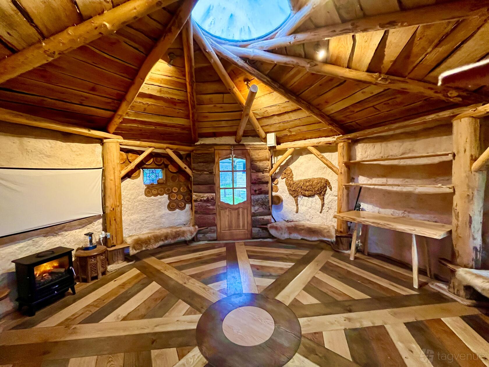 An event space in a barn with exposed timber beams, circular wooden floor pattern, and log walls at Cadbury Alpacas.