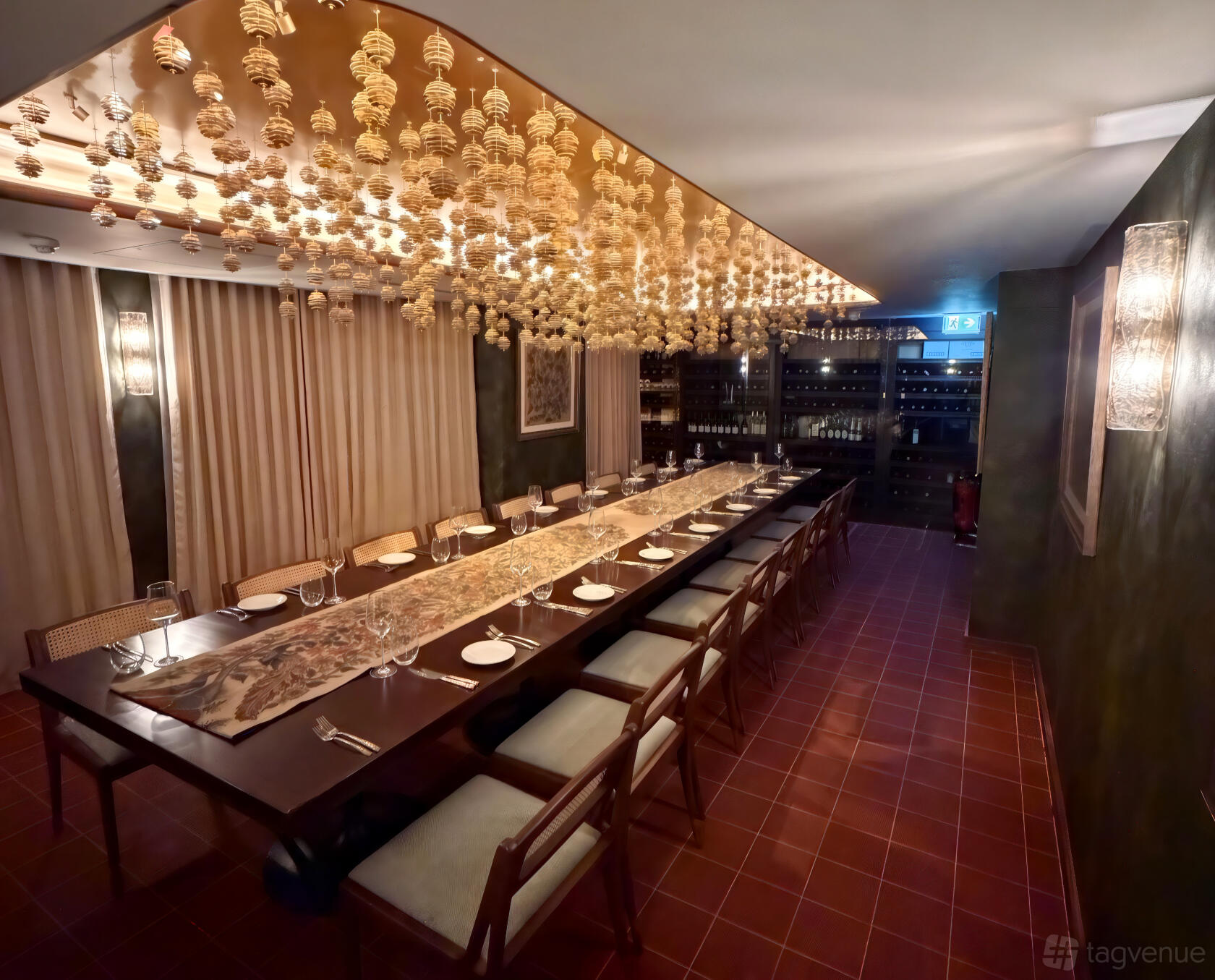 A private dining room with a long banquet table, hanging decorative ceiling accents, and wine shelves at Quilon.