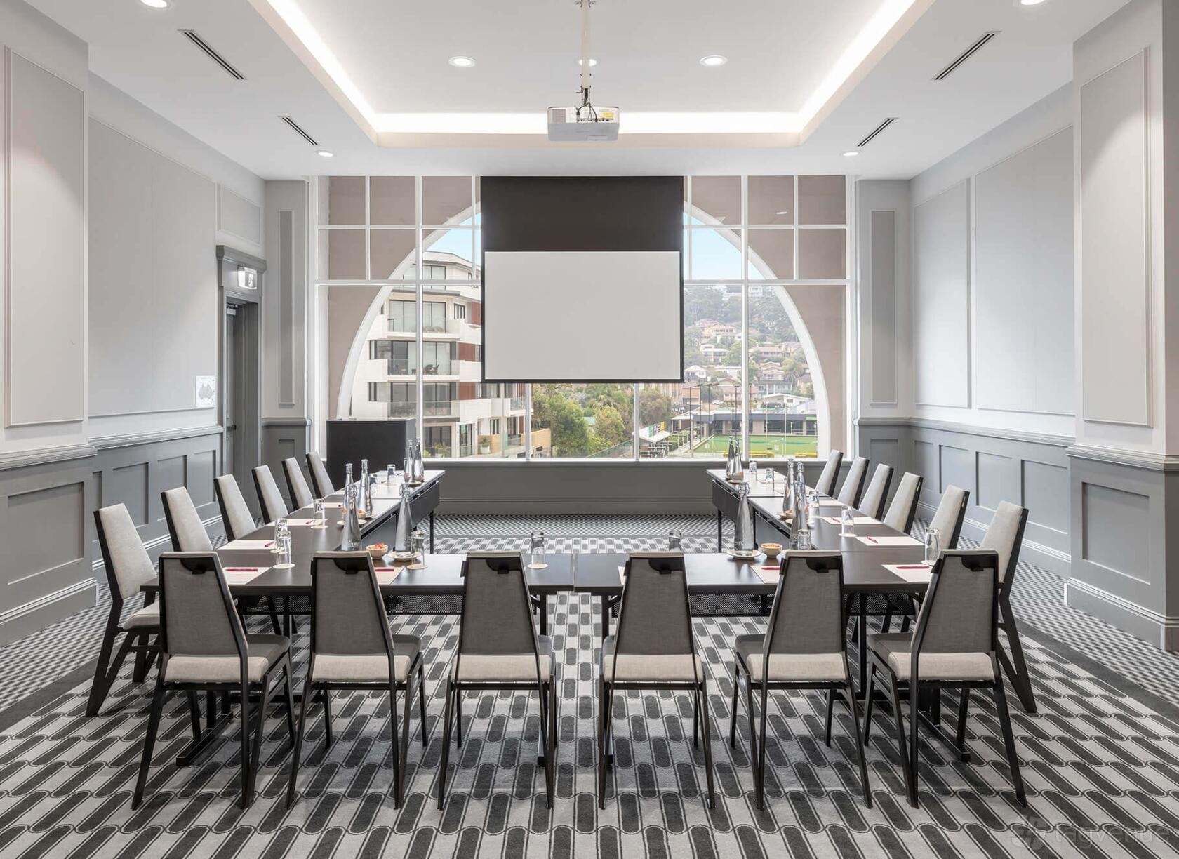 An event space in a hotel with U-shaped tables, a ceiling-mounted projector, and large arched windows at Crowne Plaza Terrigal Pacific.