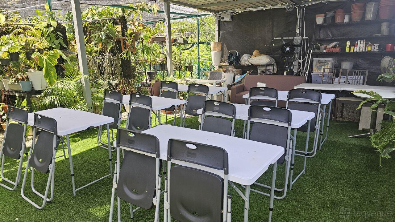An outdoor event space with white folding tables, black chairs, artificial grass, and potted plants at Baba Potter.