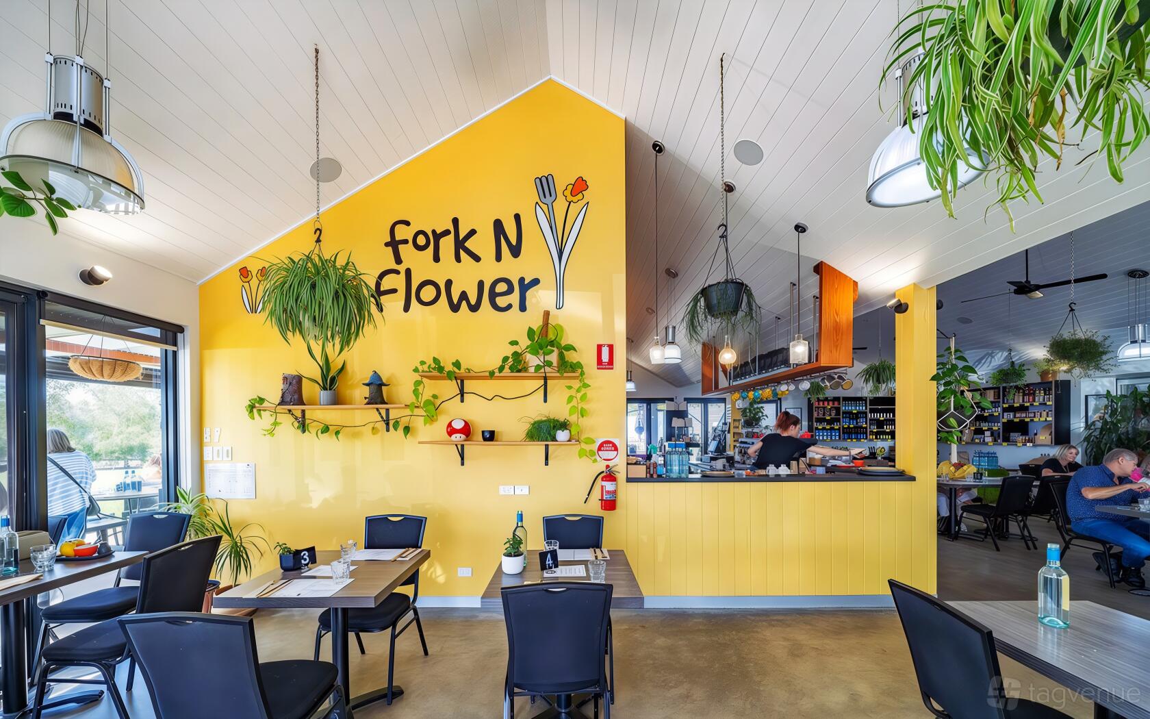 A cafe with yellow accent walls, hanging plants, and black chairs at Fork N Flower.