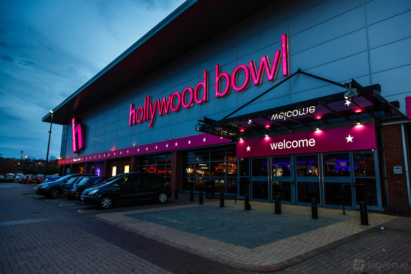 An event venue with a bright pink neon sign, glass entrance doors, and adjacent parking at Hollywood Bowl Birmingham Rubery.