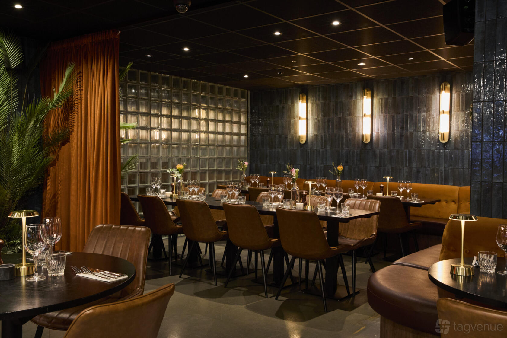 A restaurant dining room with brown leather chairs, dark tiled walls, and wall-mounted lighting at KöD Soho.