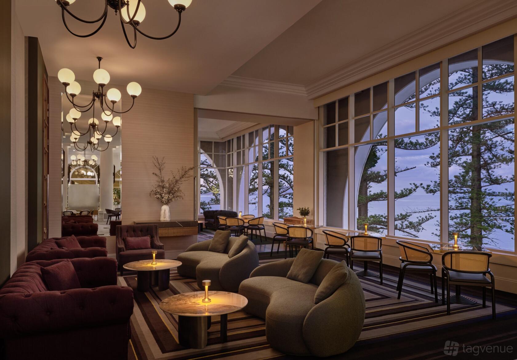 An event space with plush lounge seating, round wooden tables, and large windows overlooking trees at Crowne Plaza Terrigal Pacific.
