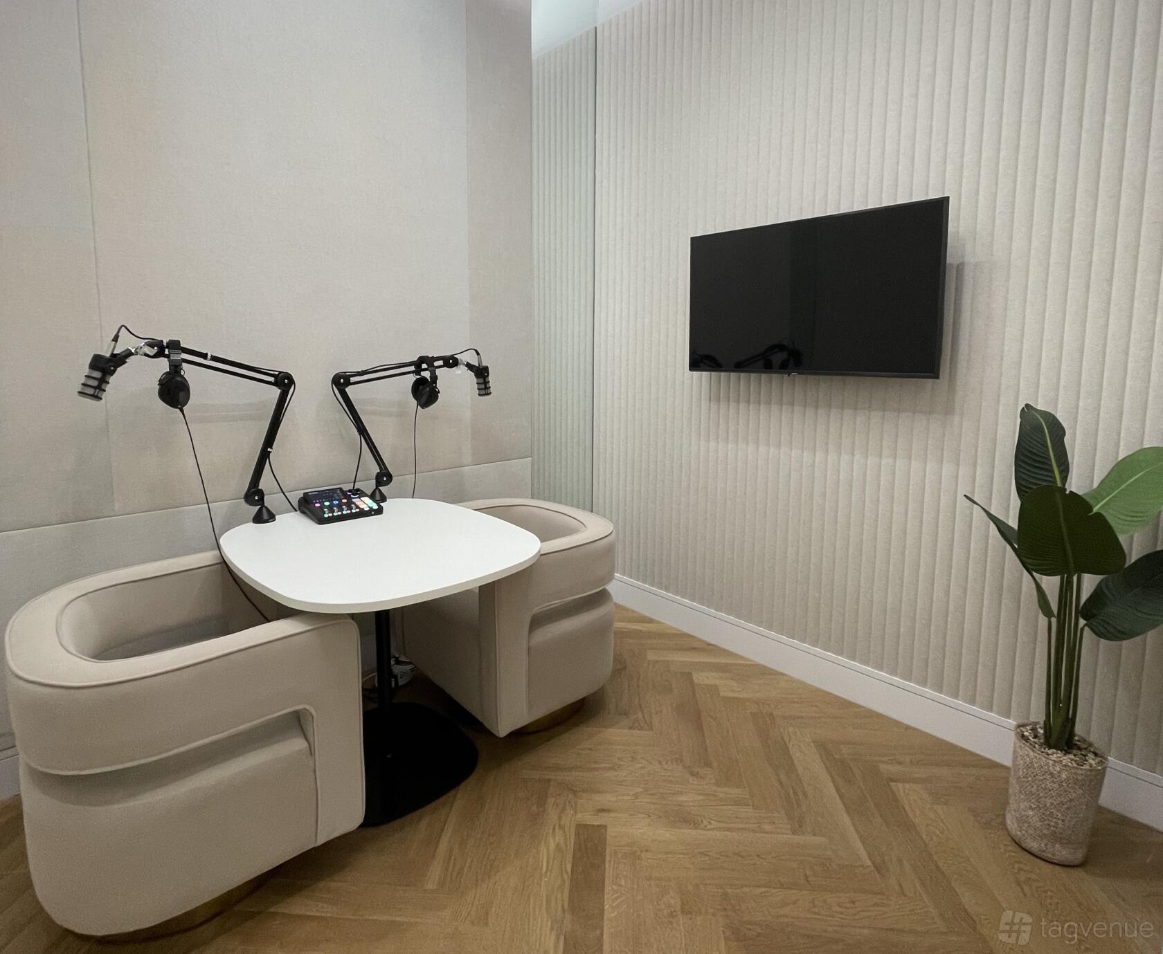 A podcast studio with two armchairs, microphones on adjustable arms, a mixing console, and a wall-mounted TV at Frederick's Place.