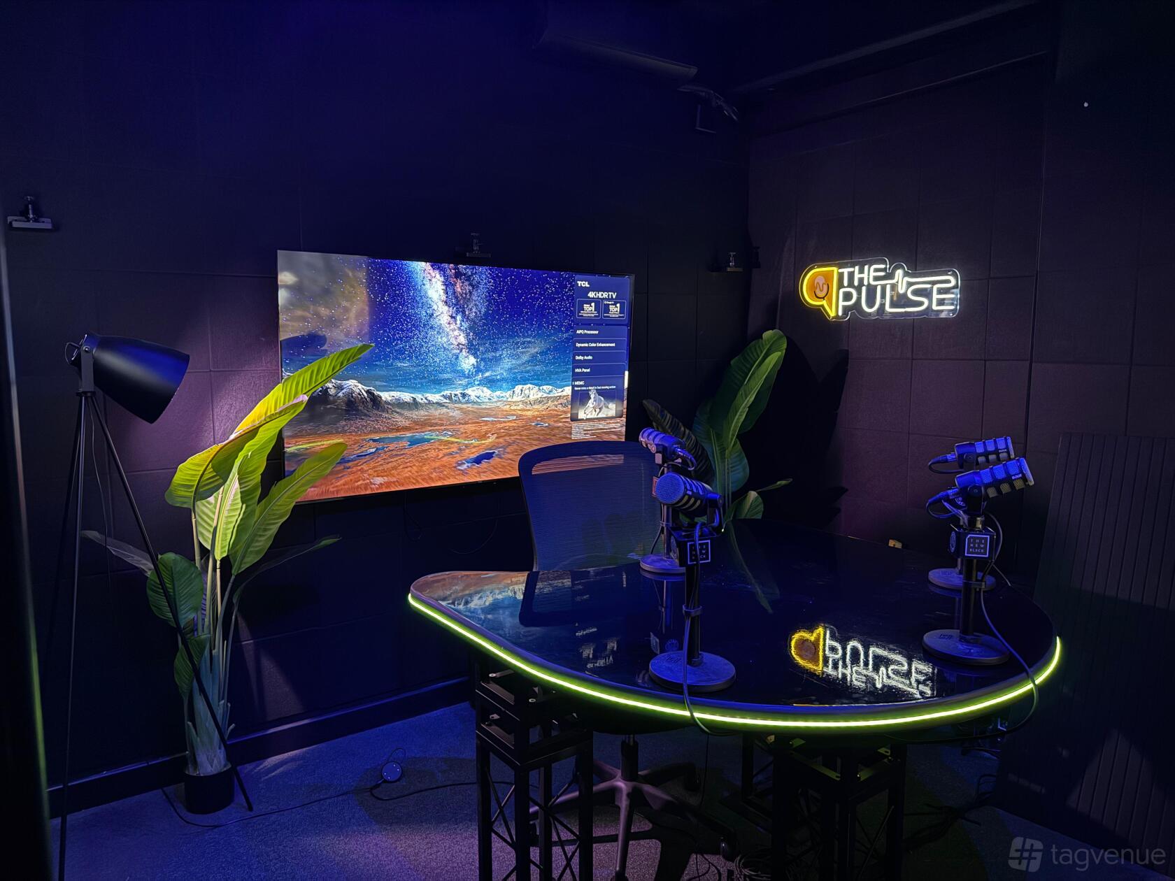 A podcast studio with a glossy black table, mounted microphones, a large display screen, and neon signage at THE NEW BLXCK.