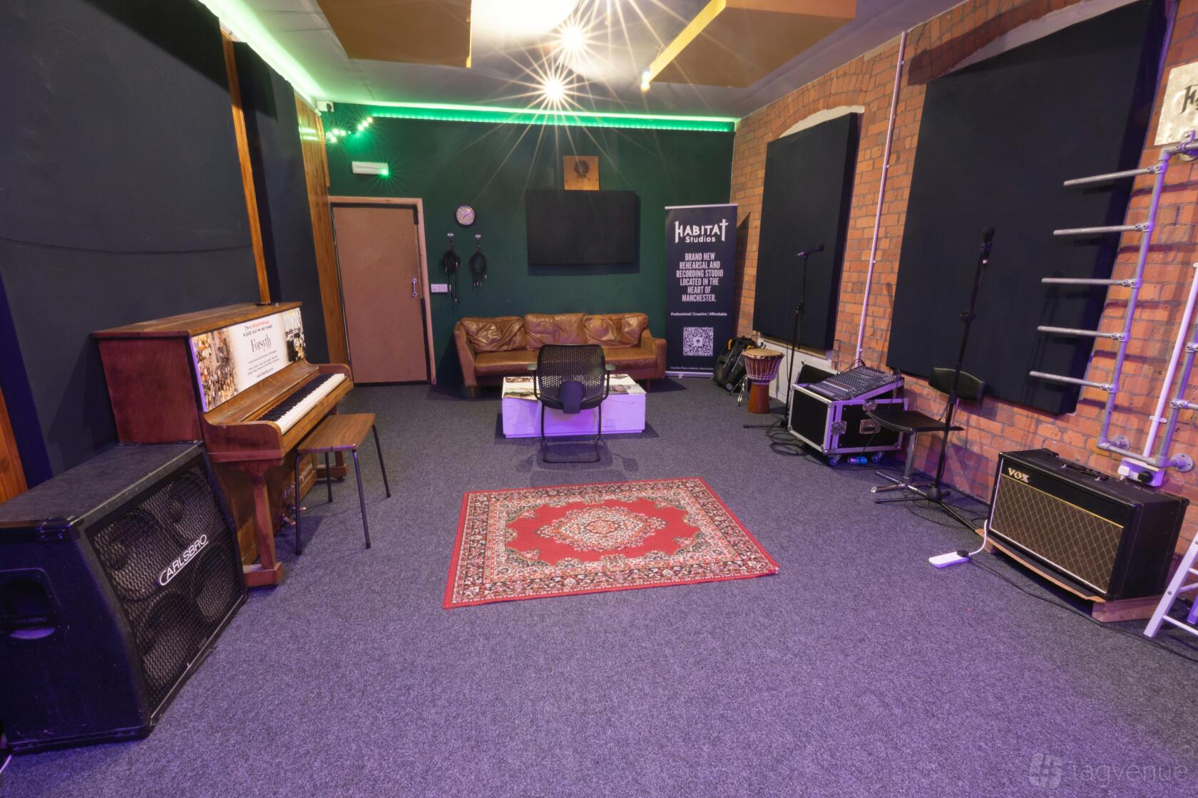 Studio 1 at Habitat Studios with upright piano, amps, exposed brick, and patterned rug