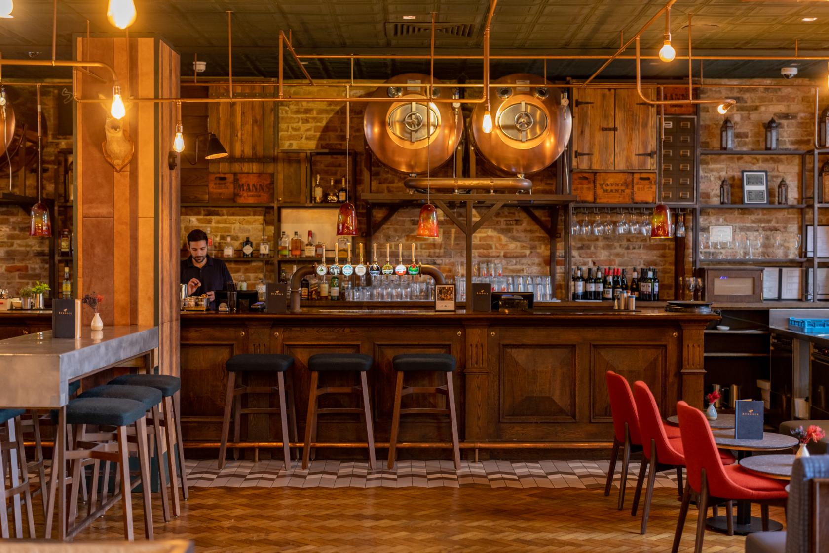An event space in a pub with exposed brick walls, copper brewing tanks, and wooden bar seating at Burdock.