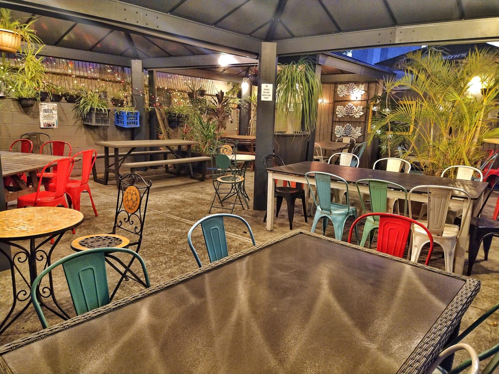 An outdoor bar space with mixed metal chairs, potted plants, and string lights at Shady Palms Cafe & Bar.