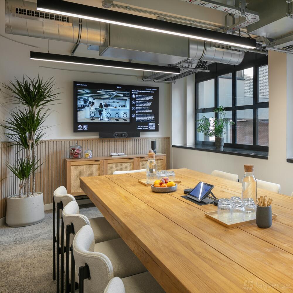 A boardroom with a wooden table, built-in screen, large windows, and potted plants at Spacemade - Beton.
