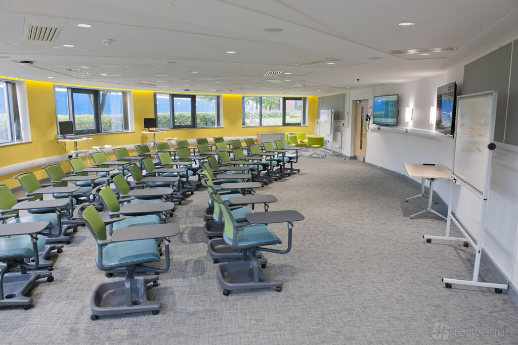 A classroom with movable green chairs, large windows, wall-mounted screens, and a whiteboard at Rothamsted Conference Centre.