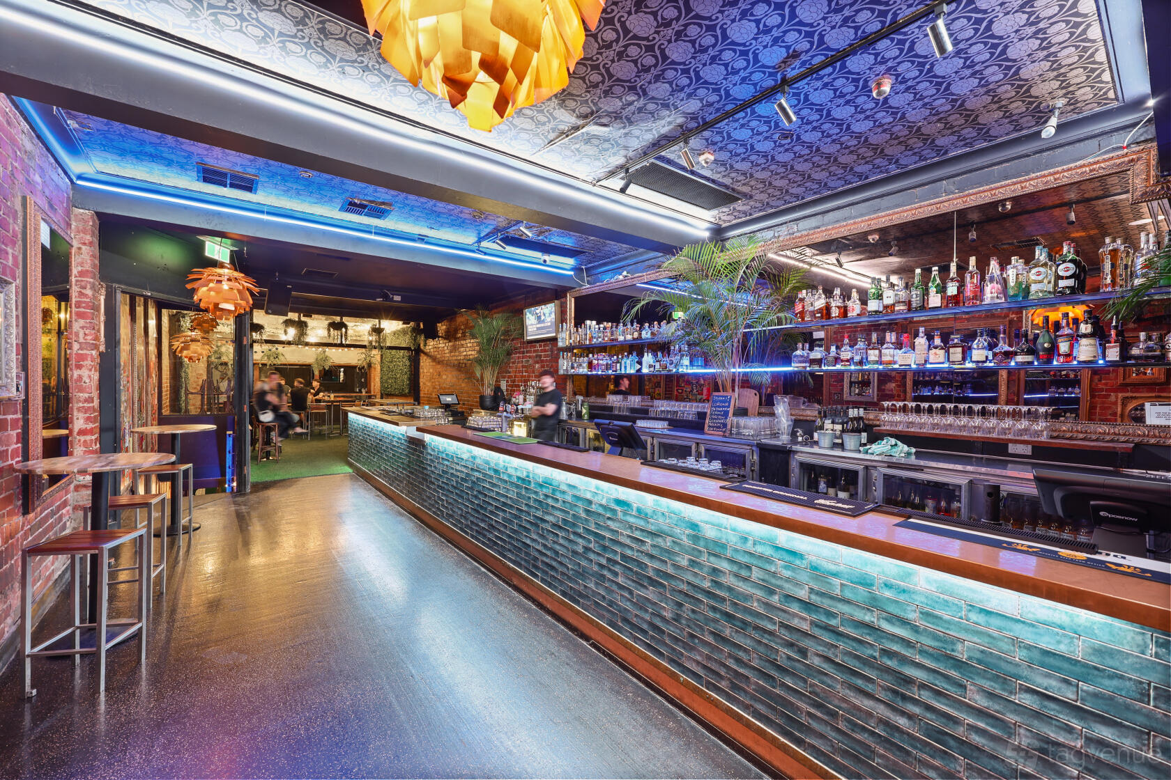 An event space in a bar with exposed brick walls, a long illuminated bar, and patterned ceiling at Jekyll & Hyde.