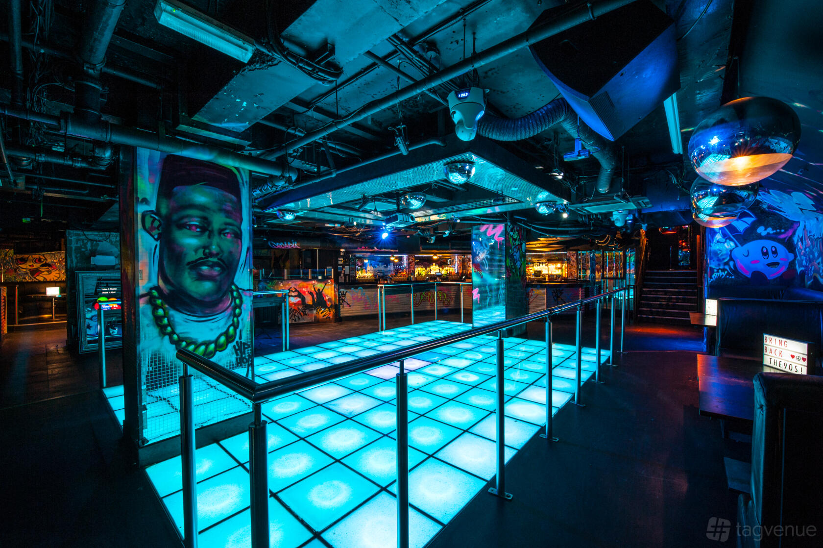 An event space in a nightclub with a glowing LED dance floor, graffiti murals, and disco balls at LUXE.