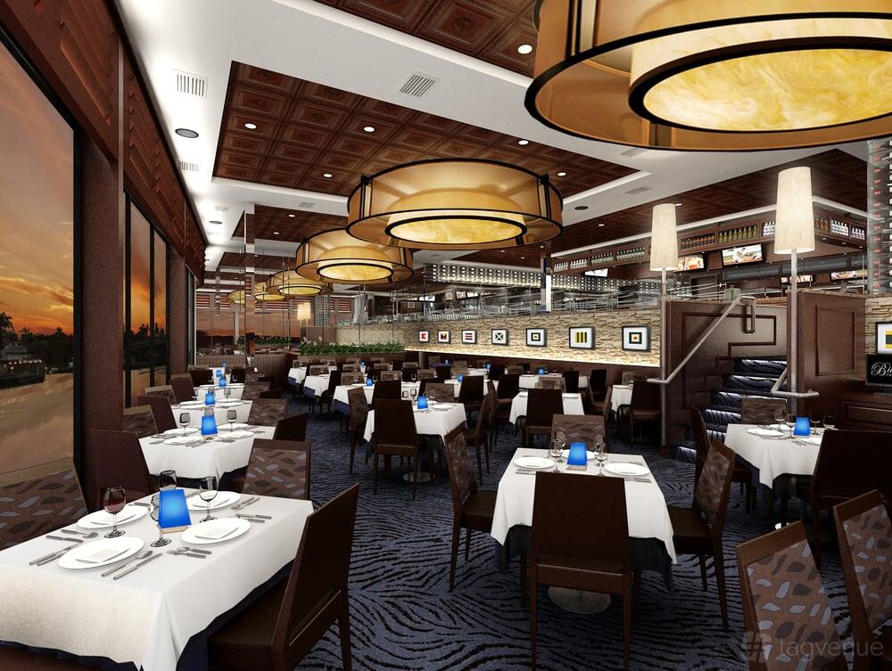 A restaurant dining area with large round pendant lights, floor-to-ceiling windows, and tables set with white linens at Billy's Stone Crab Hollywood.