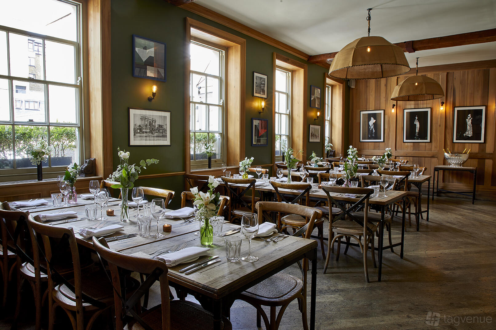 A pub dining room with wooden tables, cross-back chairs, large windows, and floral centerpieces at The Grazing Goat Marylebone.