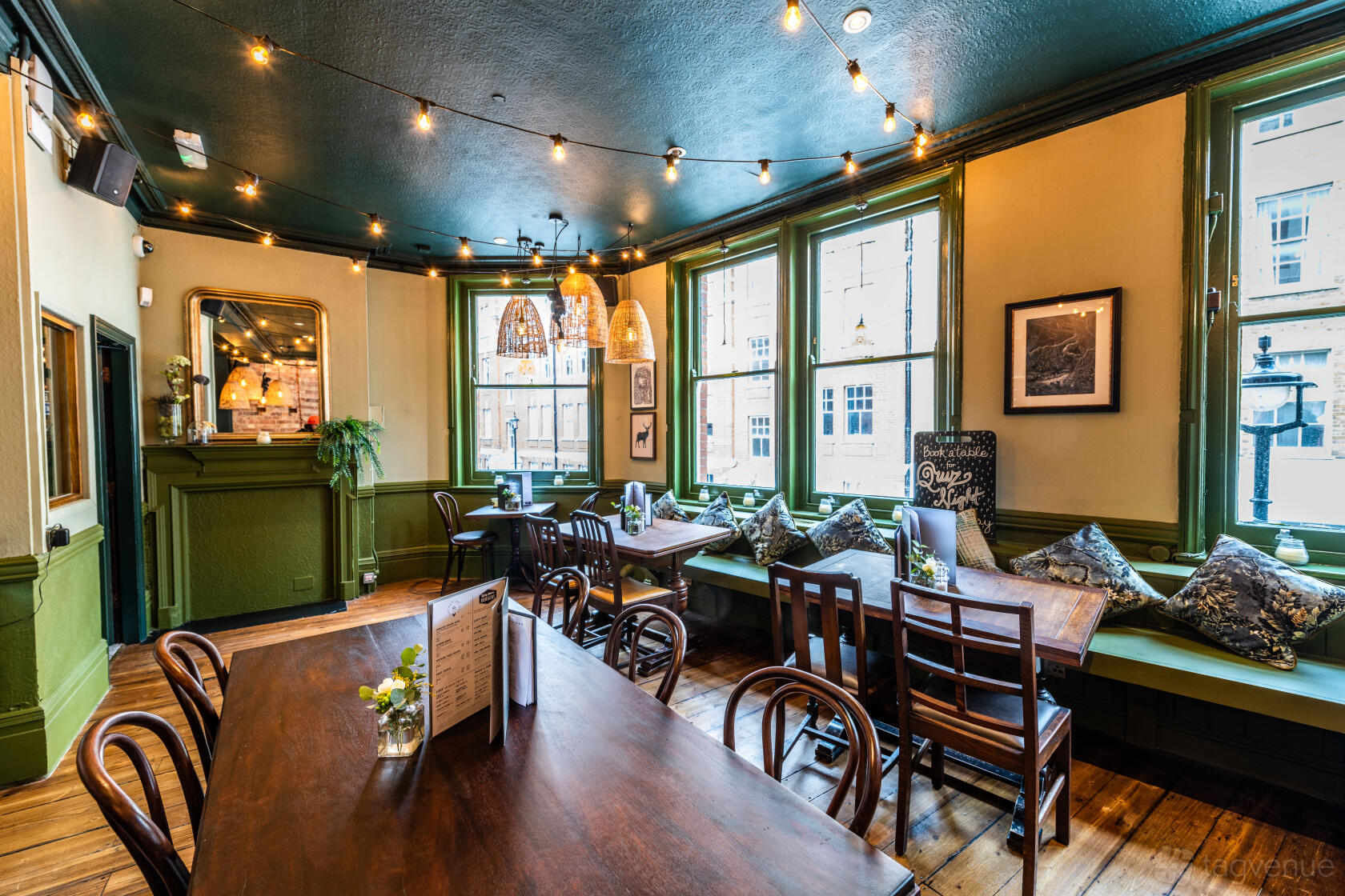 A function room with wooden floors, string lights, and window seating with cushions at The Green Man.