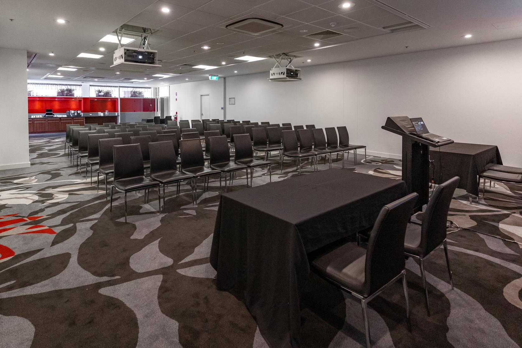A meeting room with rows of black chairs, a patterned carpet, and a presenter’s podium at Adelaide Rockford Hotel.