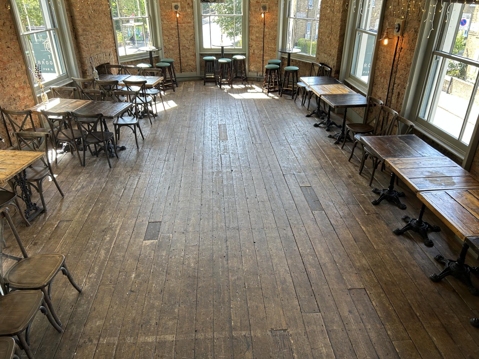 A function room with wooden floors, exposed brick walls, and large windows at The Brookmill.