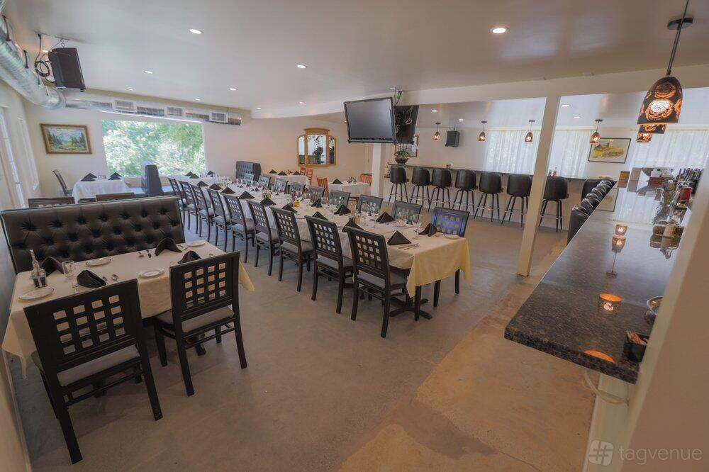 A restaurant with long banquet tables covered in white linens, dark chairs, and a marble bar at Palermo Italian Restaurant.