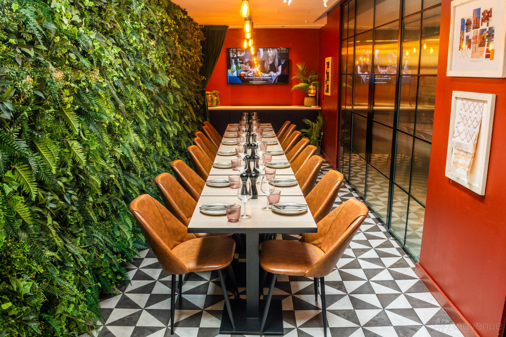 A dining room with a long table, tan leather chairs, geometric flooring, and a living plant wall at Hyatt Place London City East.