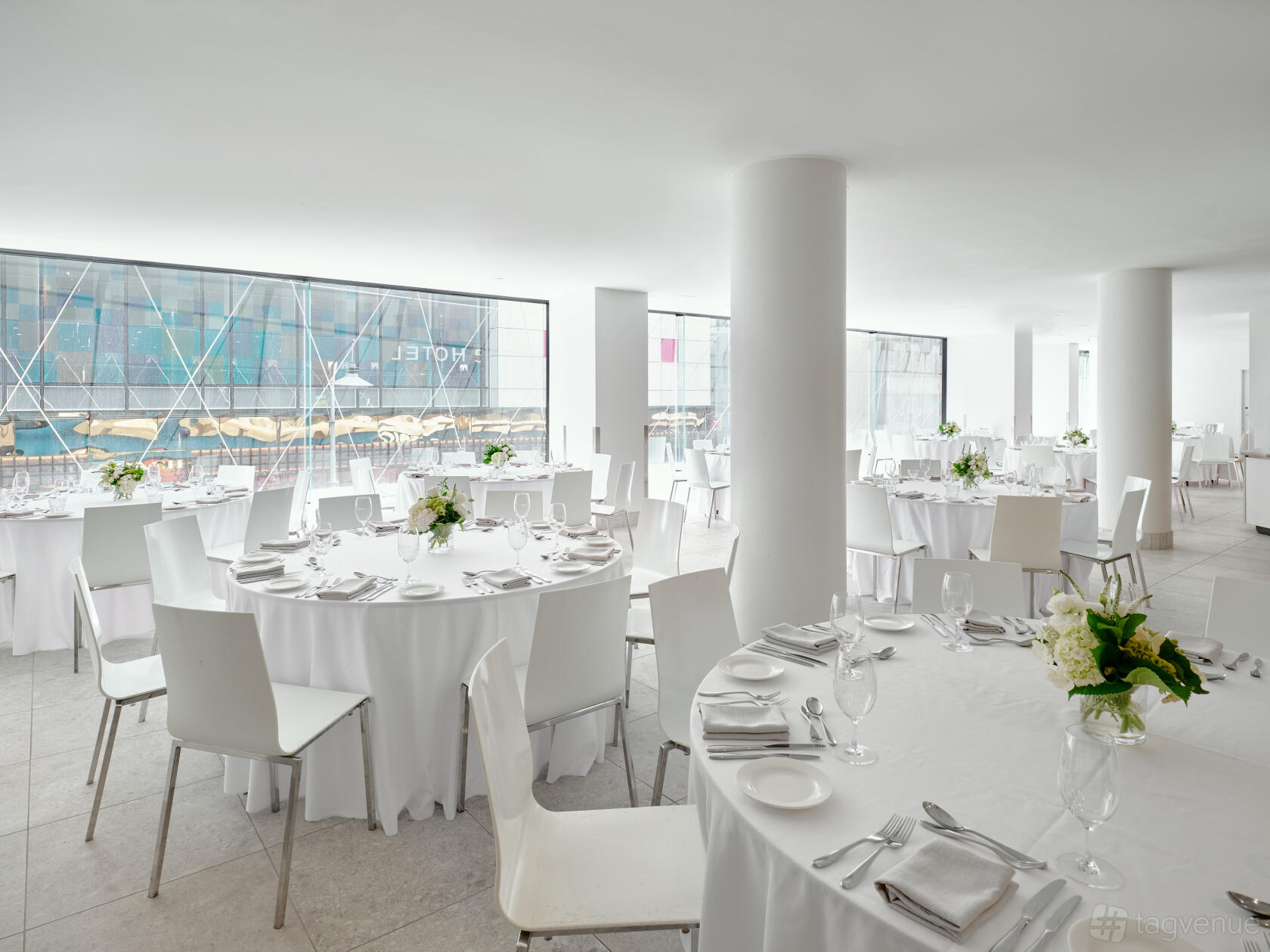 An event space with floor-to-ceiling windows, round tables with white linens, and minimalist decor at Pullman Melbourne City Centre.