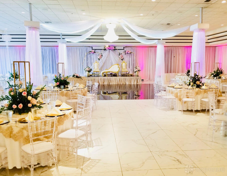 An event hall with marble floors, draped white ceiling fabric, round tables with gold linens, and floral centerpieces at The Terrace Banquet Halls.