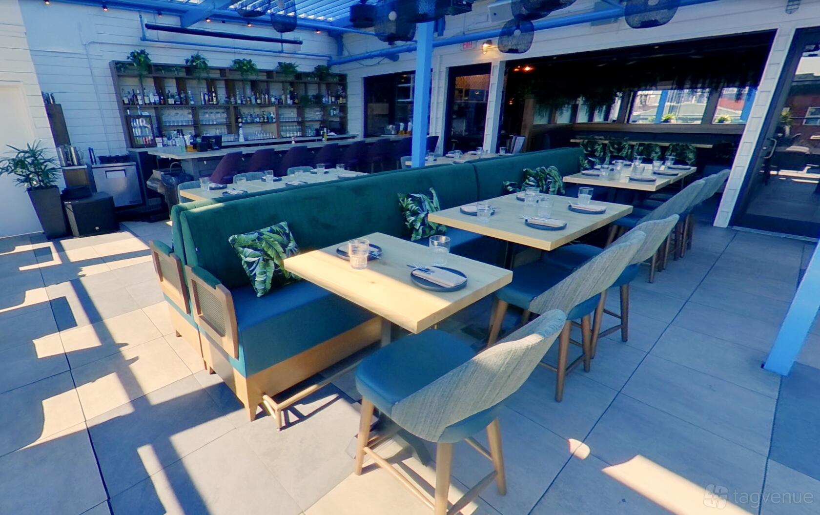 A restaurant with colorful cushioned banquettes, wooden tables, and a backlit bar at Buena Vida Gastrolounge.