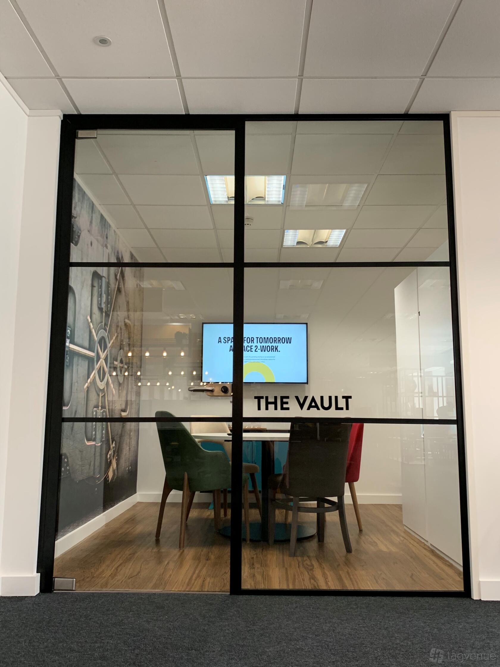 A meeting room with a wall mural of a safe door, a screen, and colorful chairs at 2-Work Bank House Leeds.