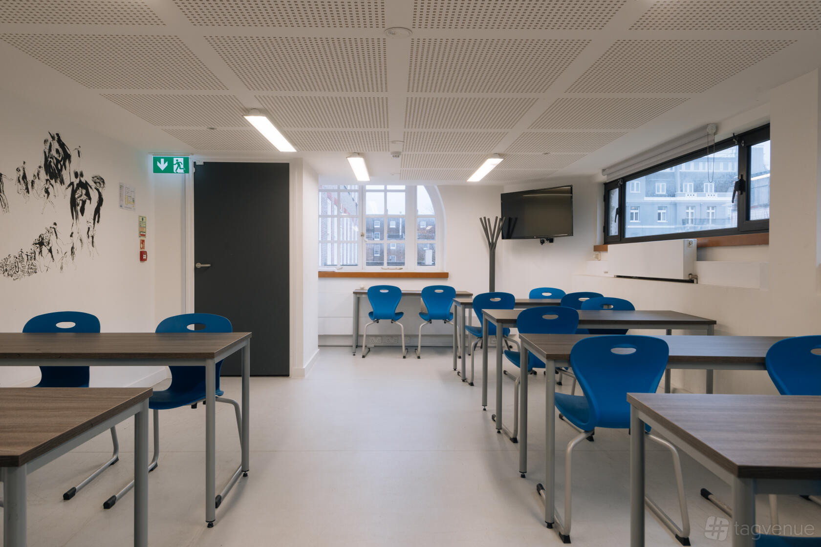 A classroom with blue chairs, rectangular tables, wall art, and large windows at Institut français au Royaume-Uni.
