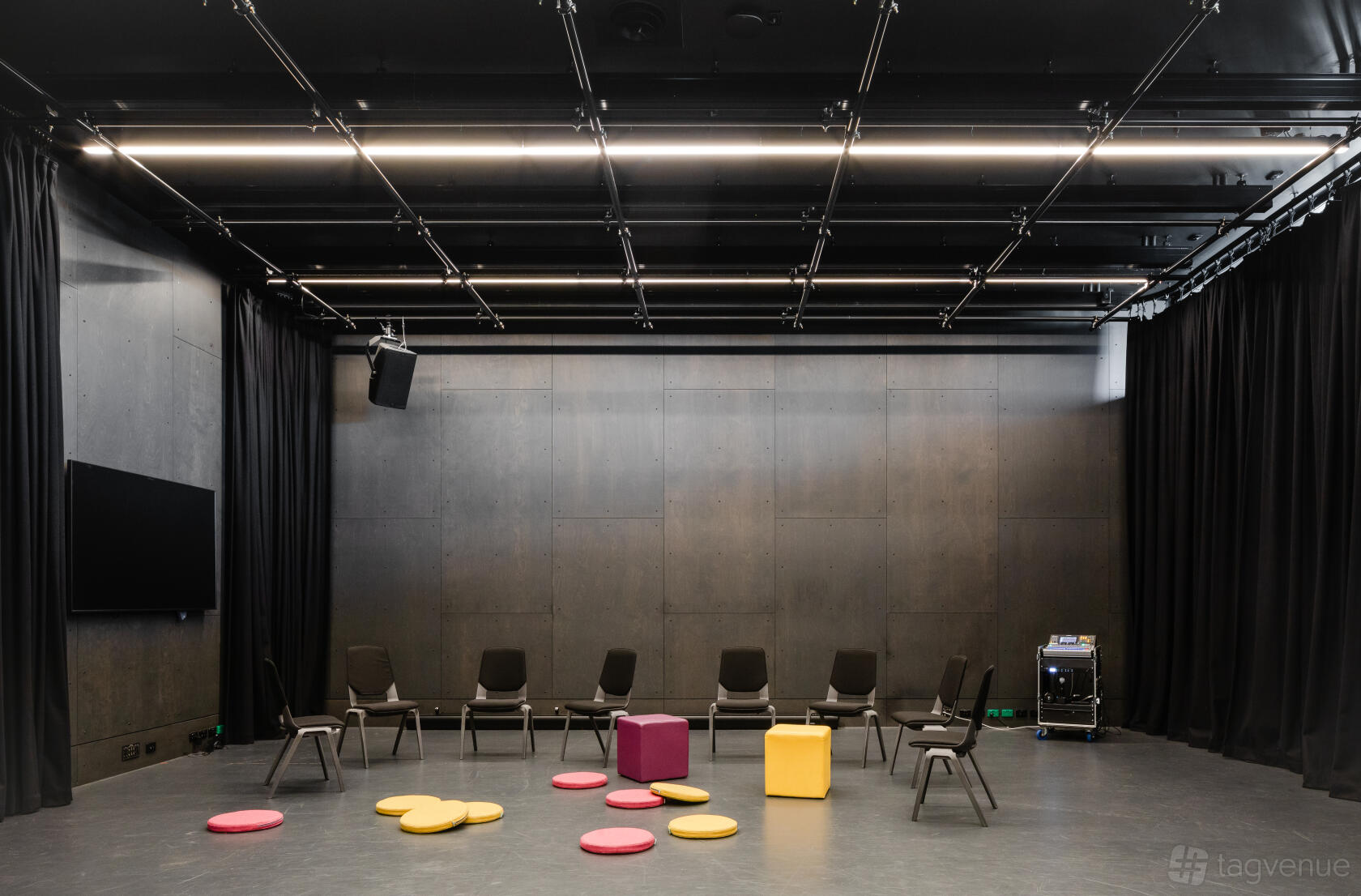A rehearsal studio with black curtains, grey walls, scattered chairs, and colorful floor cushions at Australian Theatre for Young People.