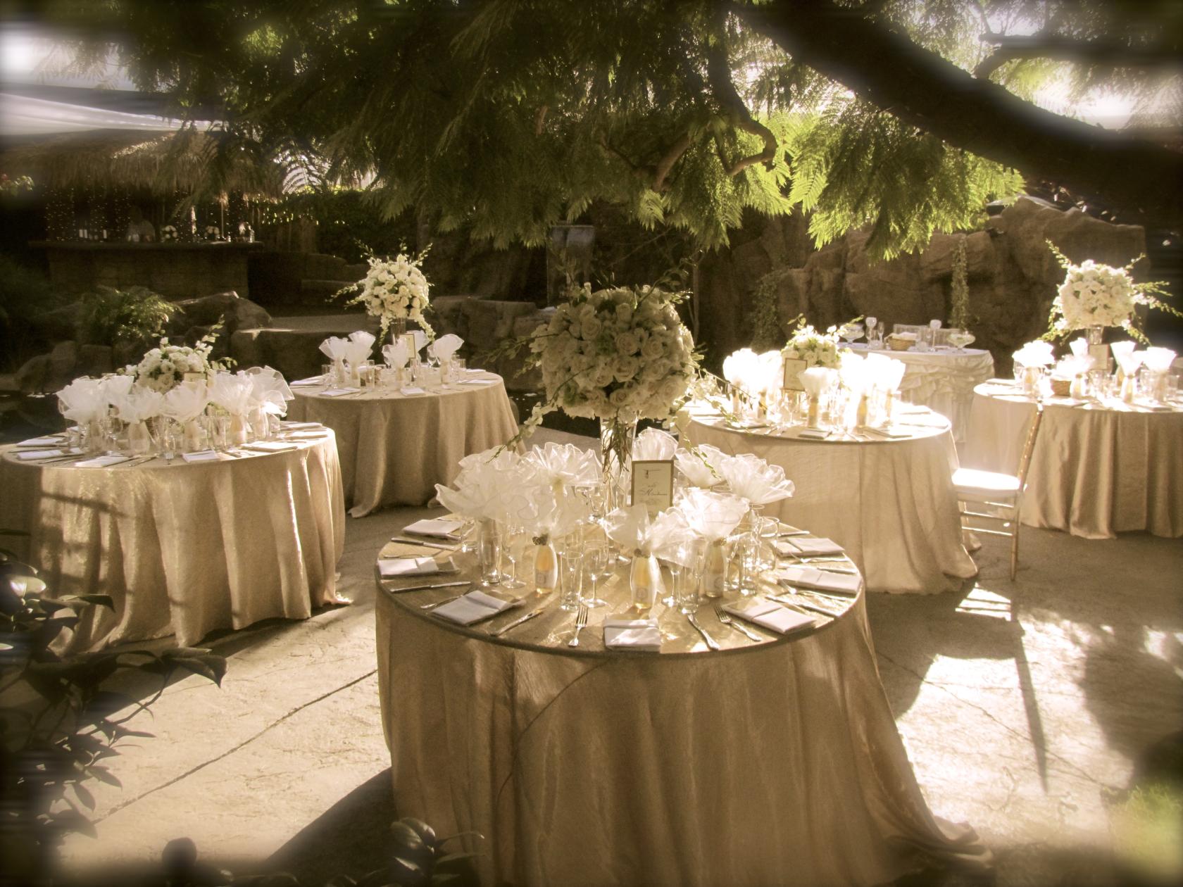 An outdoor house venue with round tables dressed in champagne linens and white floral centerpieces at Enchanted Manor.