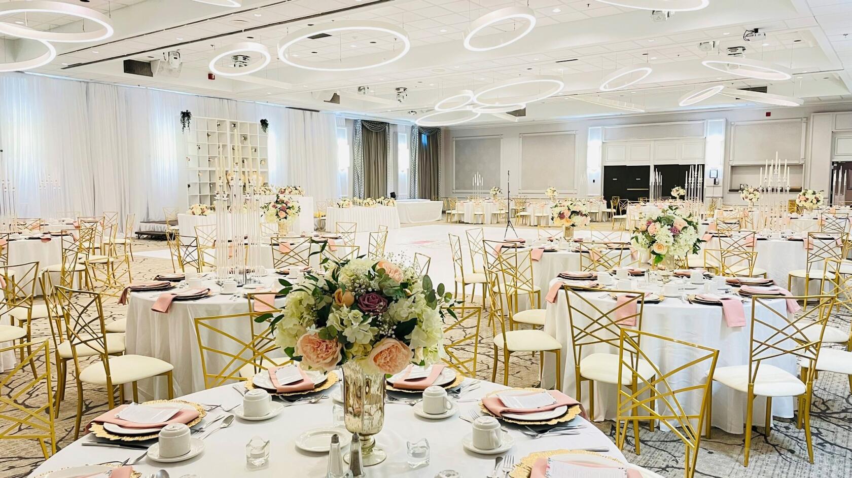 A hotel ballroom with round tables, gold chairs, floral centerpieces, and modern ring ceiling lights at CROWNE PLAZA KITCHENER-WATERLOO.