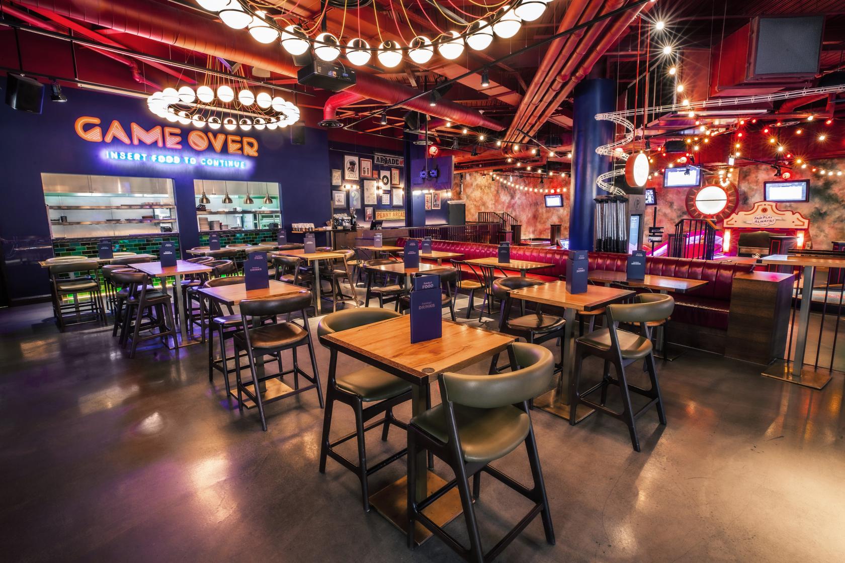 An event venue with wooden tables, modern chairs, neon lighting, and exposed ceilings at Puttshack White City.