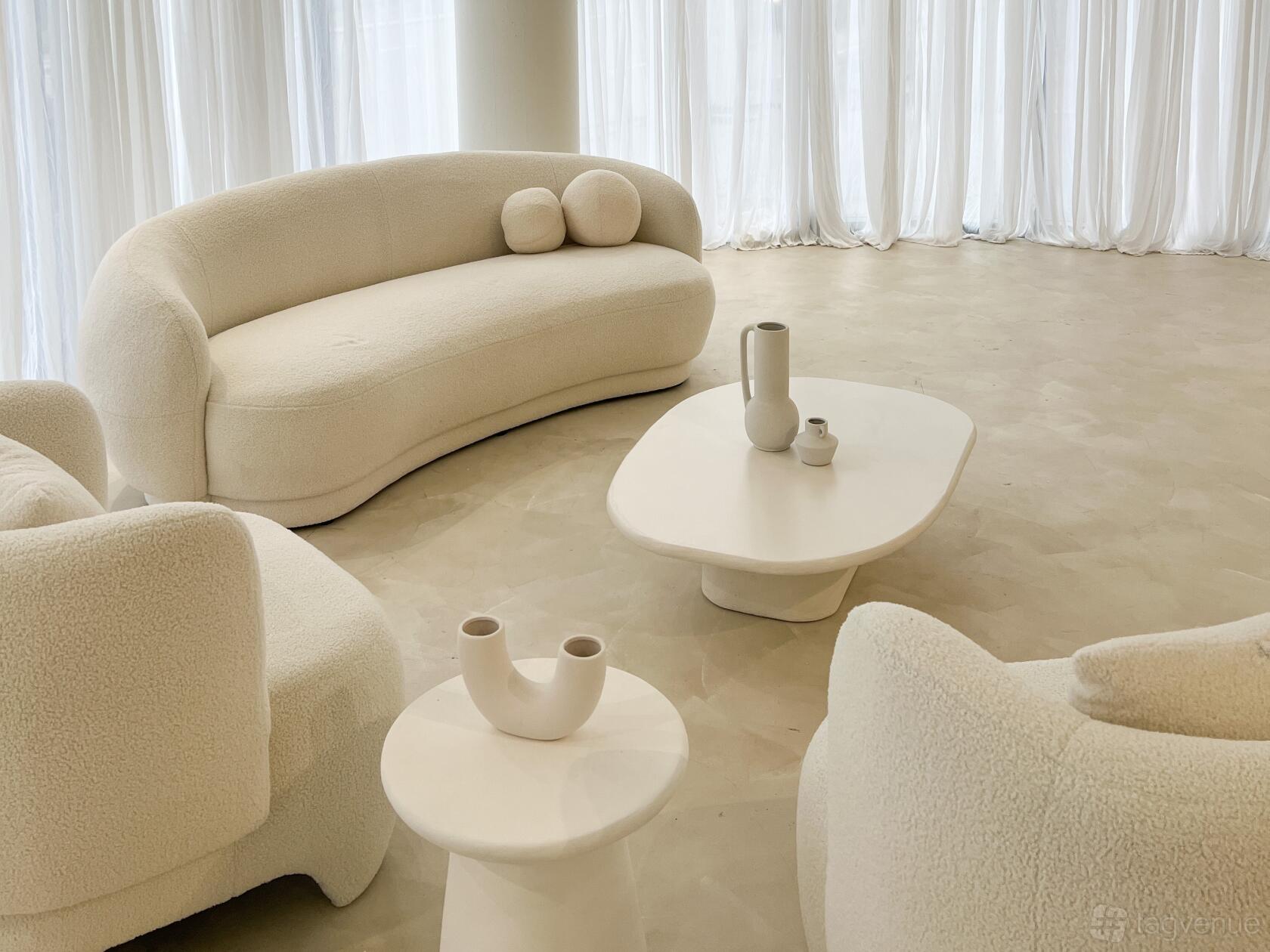 An event venue with curved white sofas, minimalist tables, and floor-to-ceiling sheer curtains at Cloud Nine Studio.