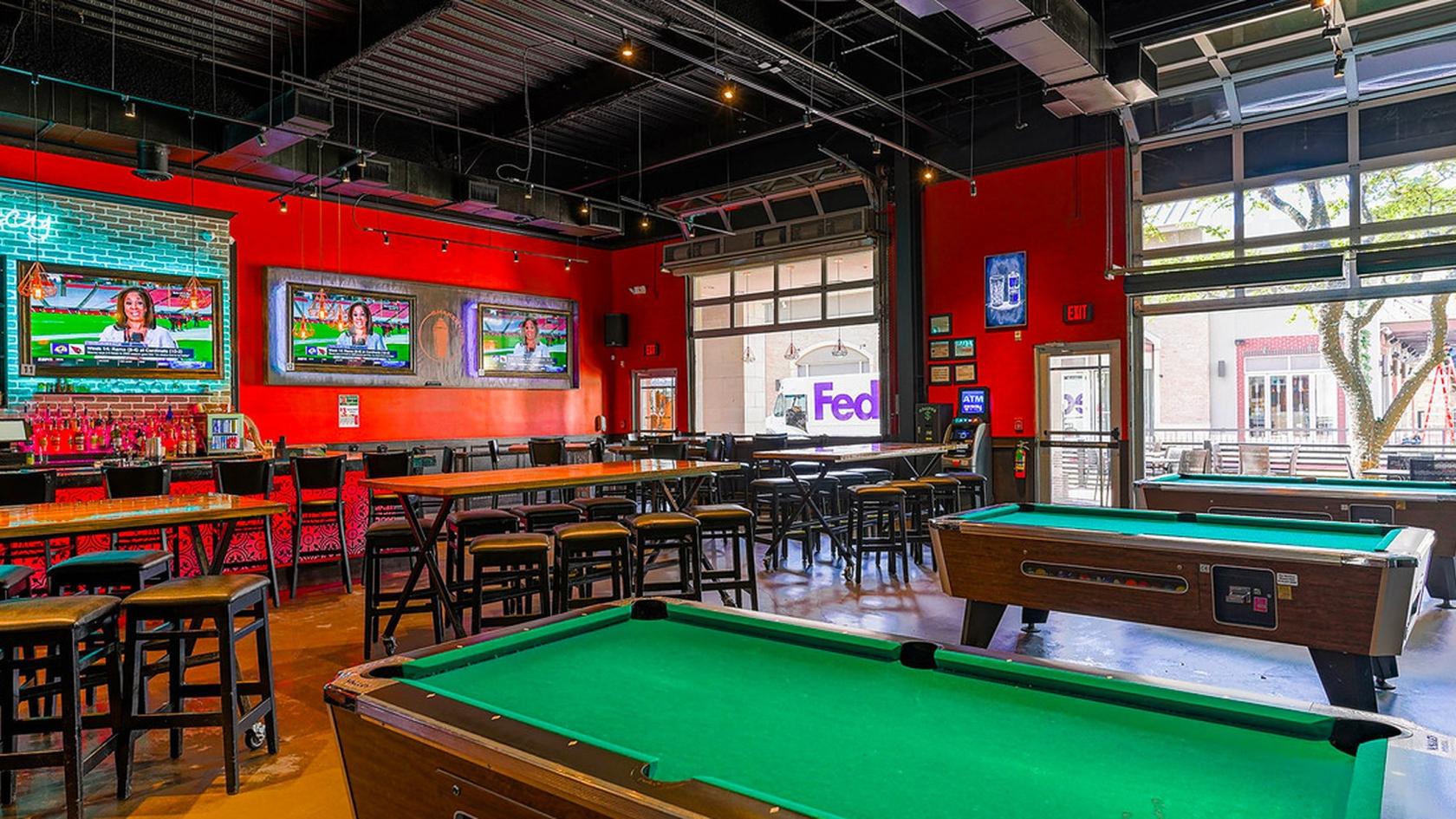 A bar with pool tables, high-top tables, red walls, and large TVs at Shakertins- Plano.