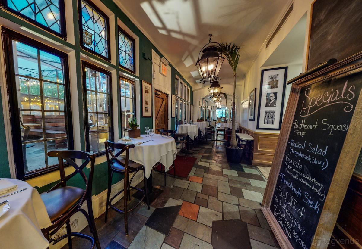 A restaurant bar area with stained glass windows, hanging lanterns, and tiled floors at Tudor City Steakhouse.