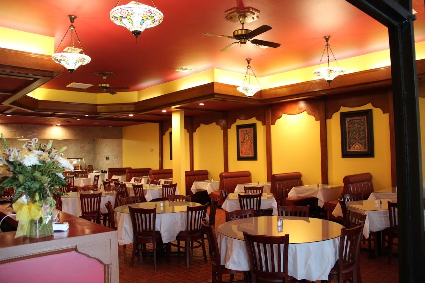 A restaurant dining area with round tables, wooden chairs, ceiling fans, and stained glass pendant lights at Curry Bliss.