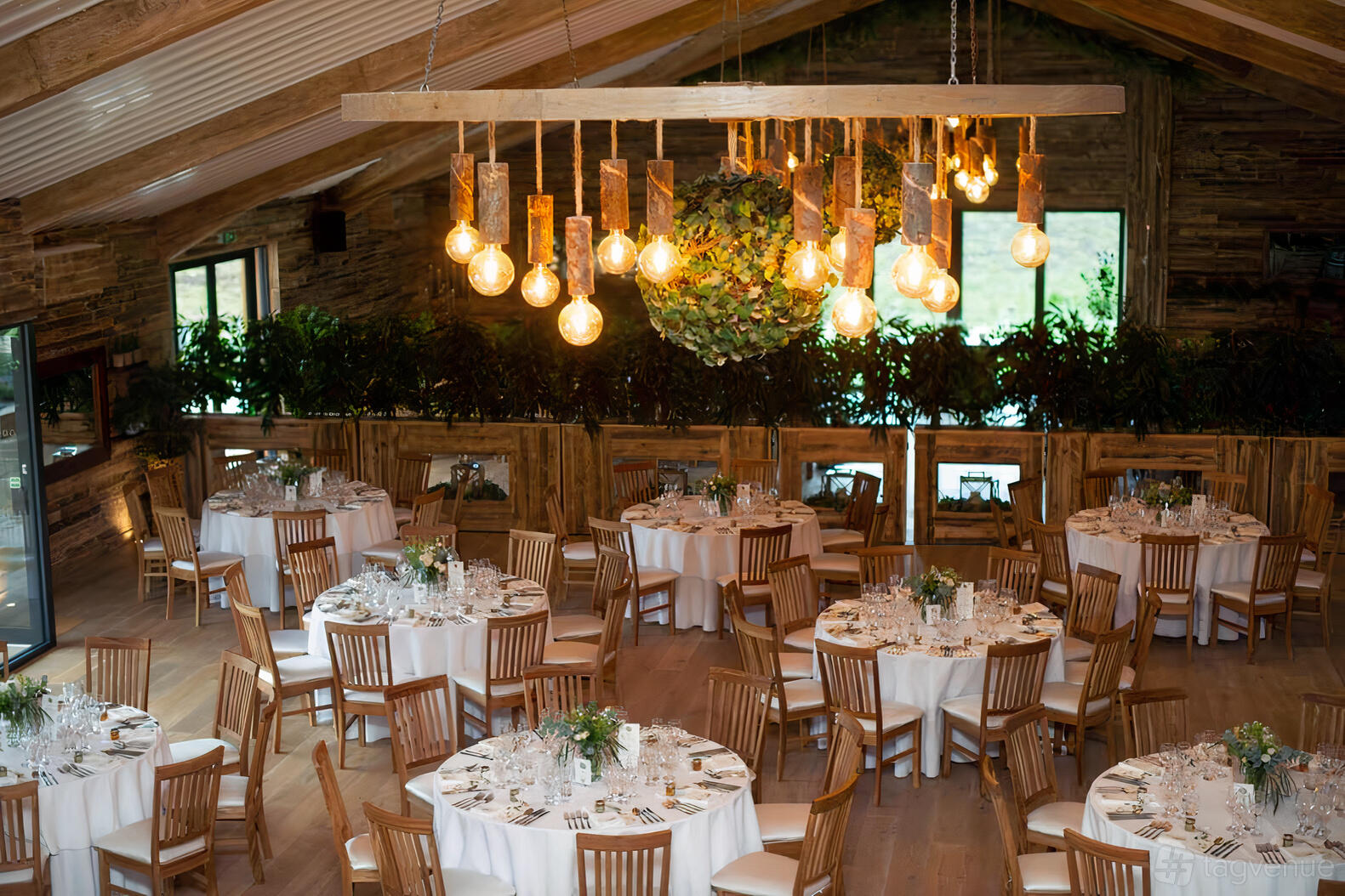 A barn venue with round tables, wooden chairs, and hanging exposed bulb lights at Woodstock Weddings and Events.