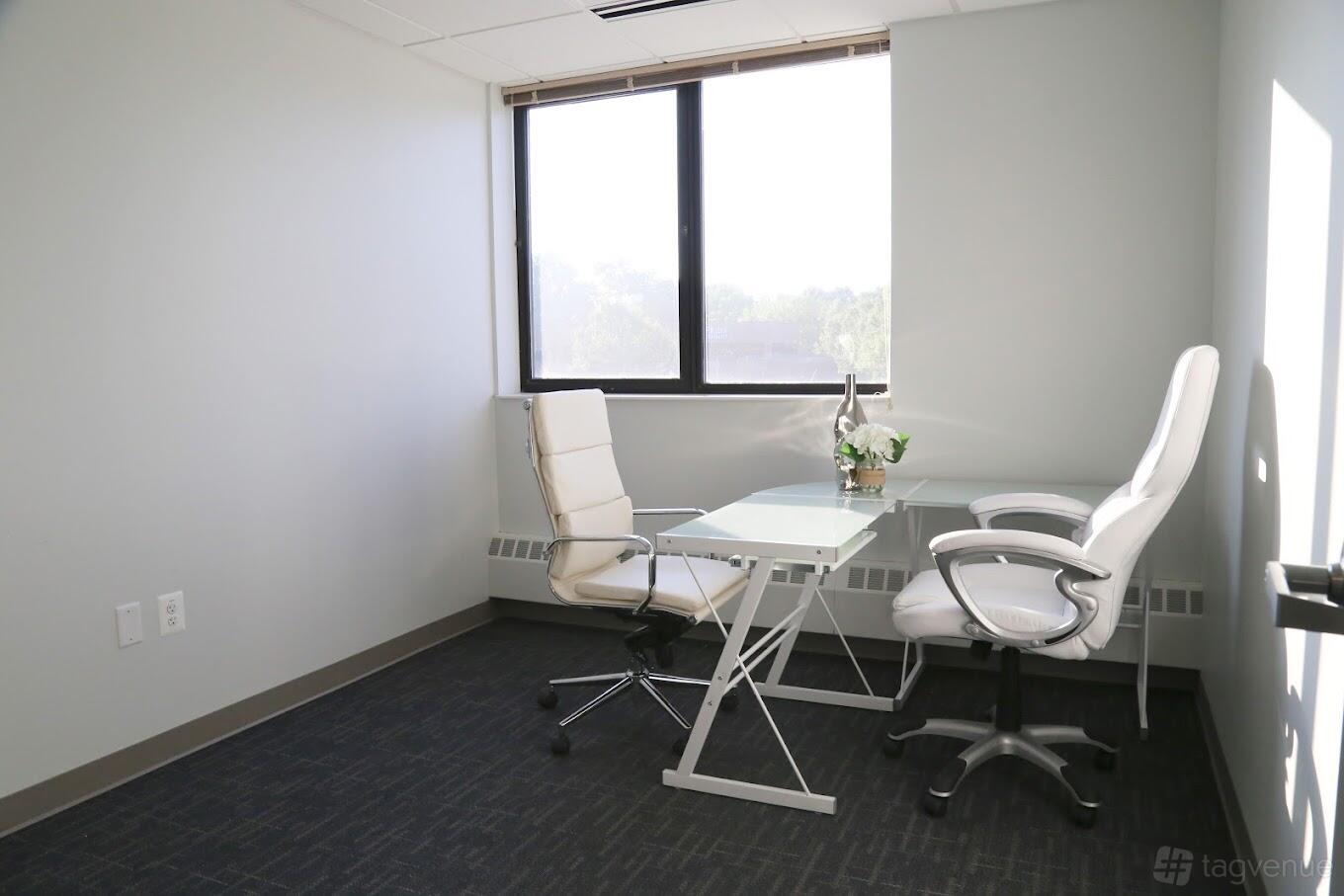 A meeting room with two white chairs, a glass desk, and a large window at Perfect Office Solutions - Silver Spring.