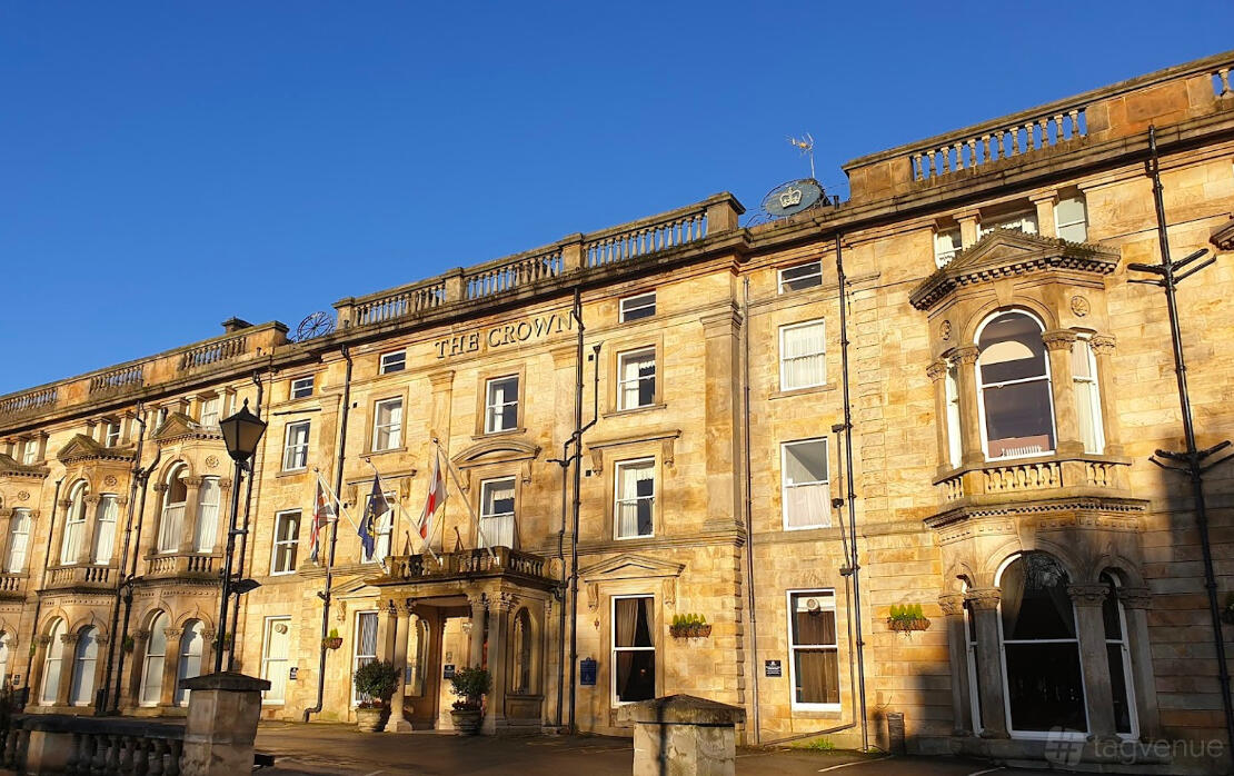 A historic hotel exterior with large sash windows, stone facade, and flags at The Crown Hotel Harrogate.