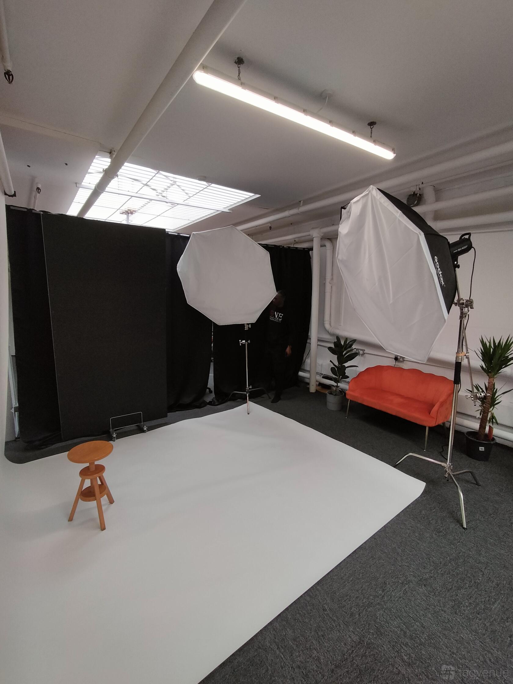 A photo studio with professional lighting equipment, black curtains, and a small orange sofa at MangoStudiosLDN.