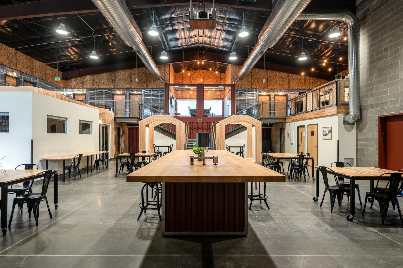 A coworking space with high ceilings, exposed ductwork, and communal wood tables at Modern Industrial Warehouse.