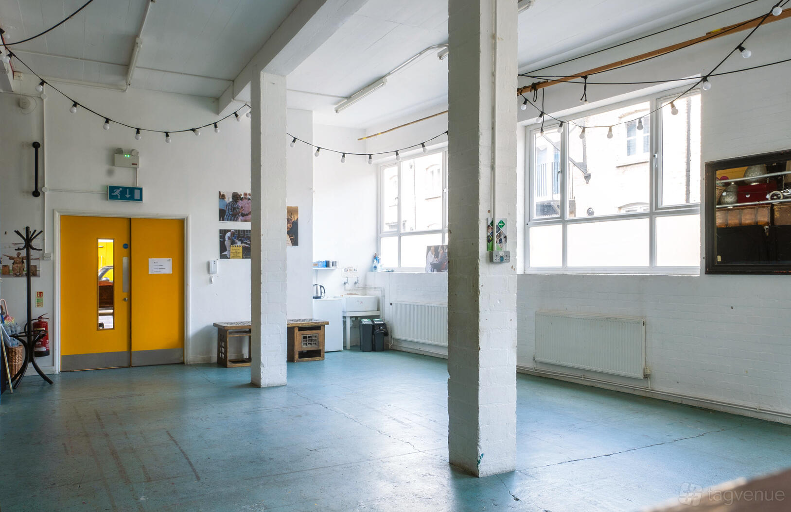 A rehearsal room with large windows, string lights, and white brick walls at London Bubble Theatre.
