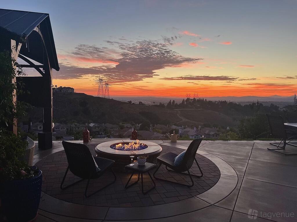 A house terrace with a circular fire pit, patio chairs, and hillside sunset views at Chateau De Soleil.