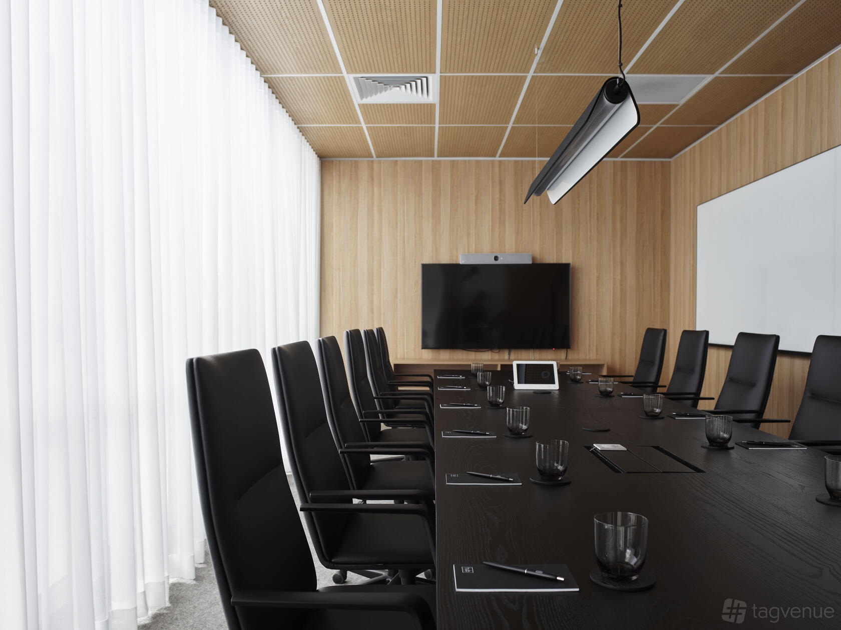 A boardroom with a long black conference table, high-back chairs, a large screen, and wood panel walls at Hub Hyde Park.