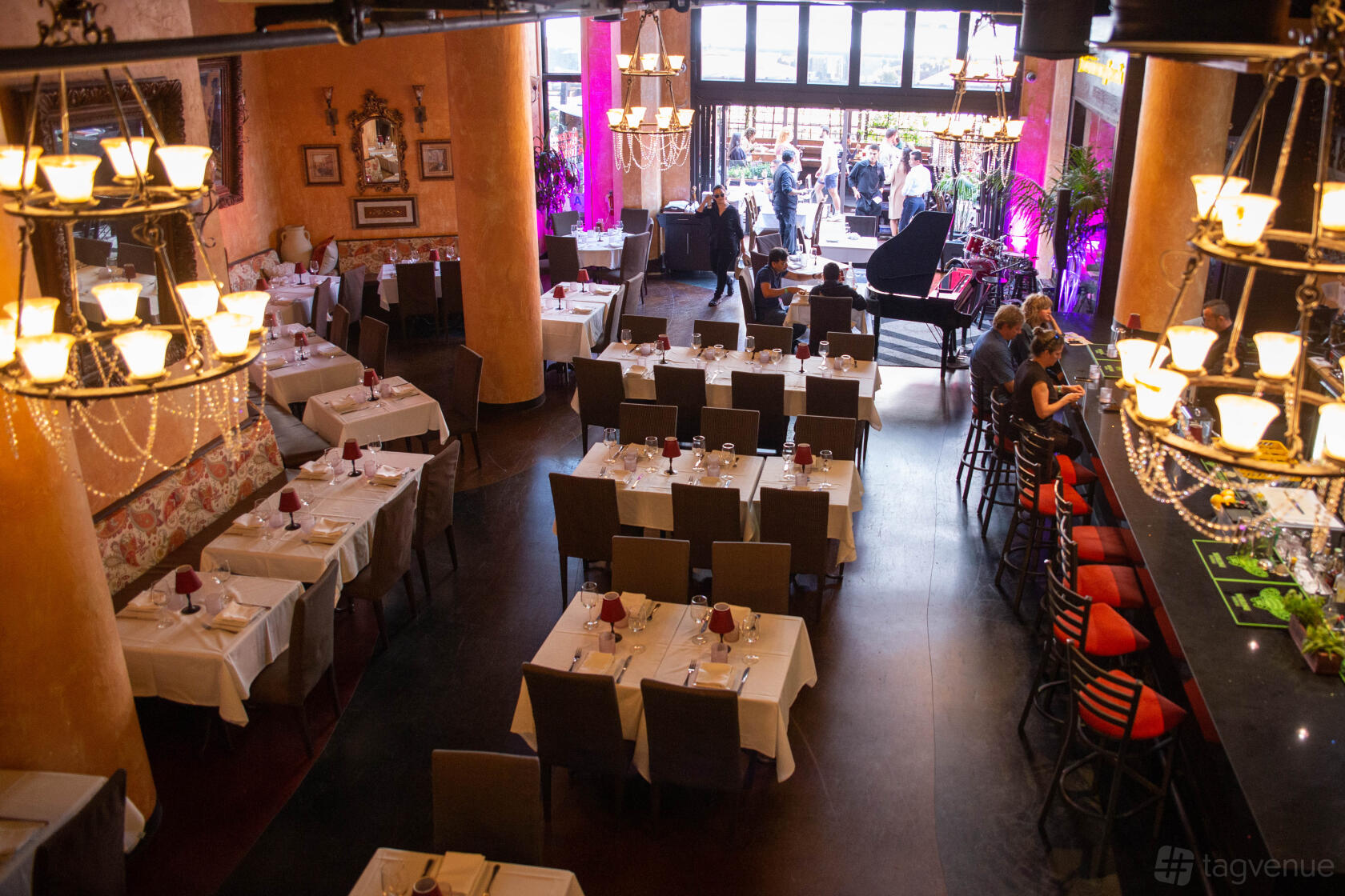 A restaurant dining area with chandeliers, white tablecloths, a grand piano, and a bar at il Sogno Italiano.