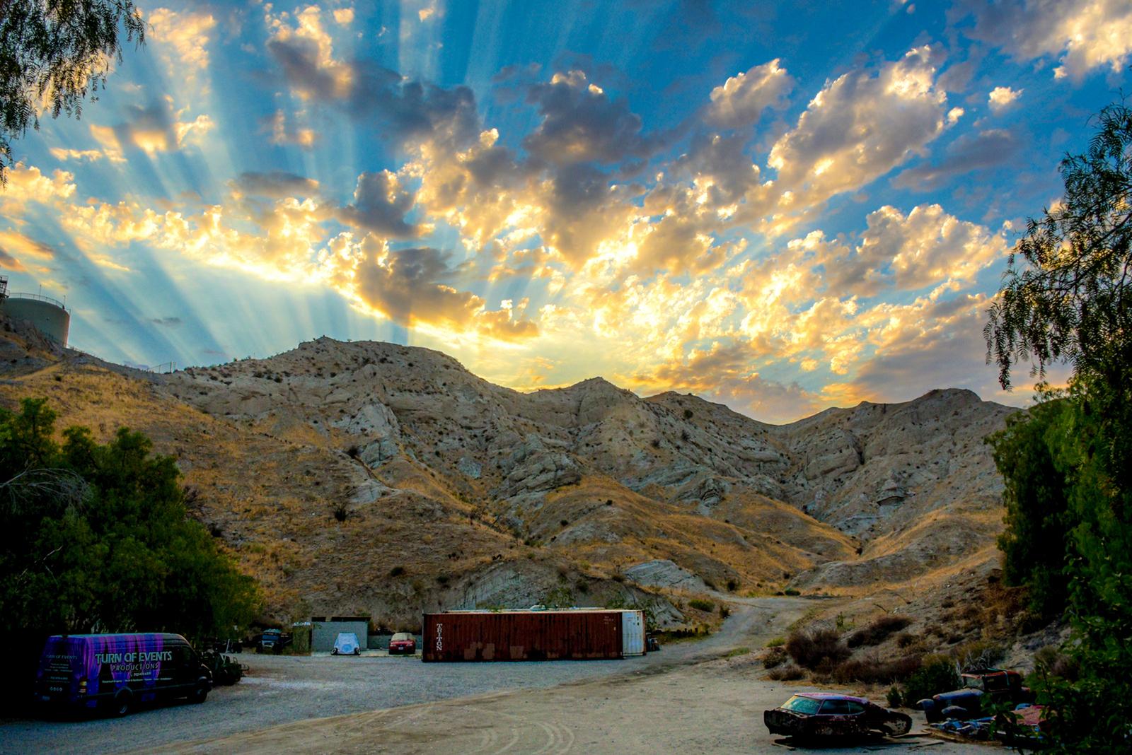 An event venue with rugged hills, scattered vehicles, and a shipping container at Tranquility Canyon Movie Ranch.