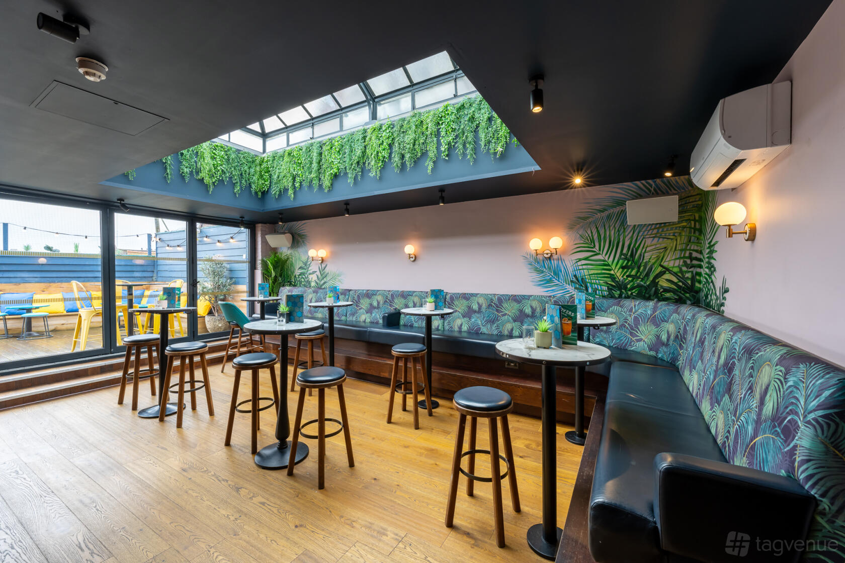 A terrace bar with skylight, hanging greenery, and tropical-print banquette seating at Be At One Chelmsford.