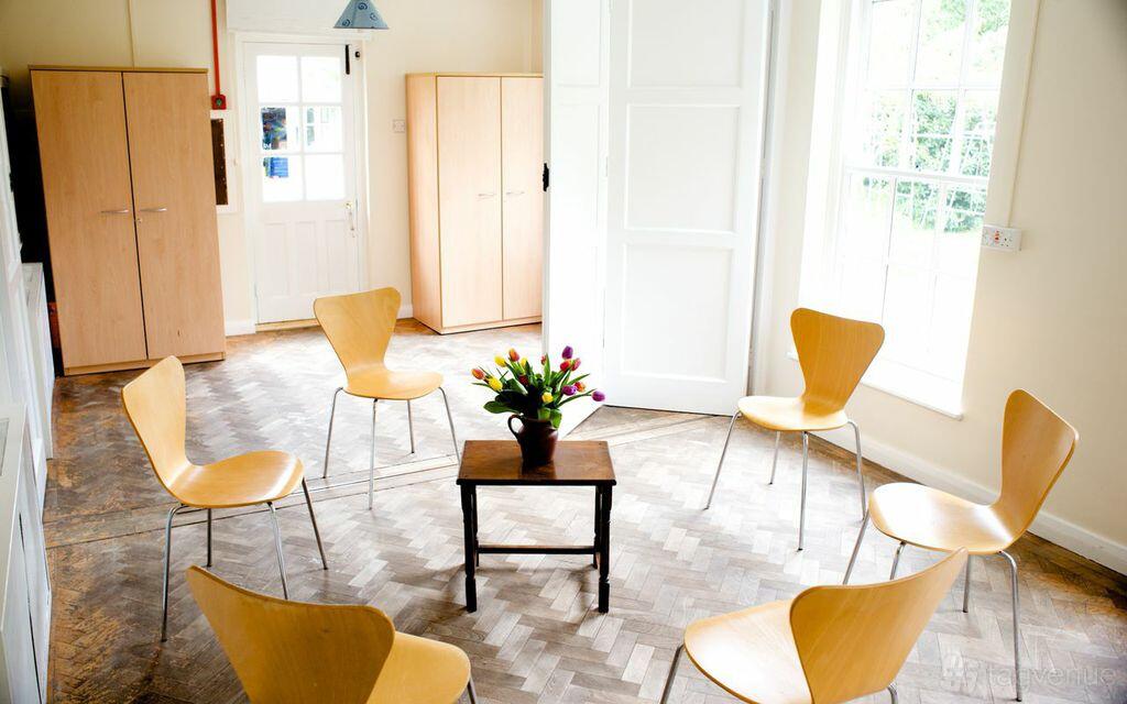 A meeting room with six wooden chairs arranged in a circle around a table with flowers at Brentford & Isleworth Quaker Meeting House.